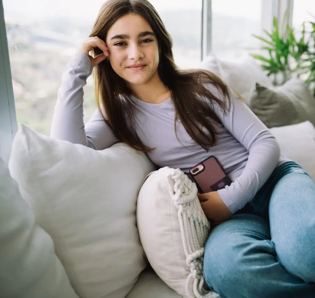 Smiling teenager girl looking at camera and smiling while holding a cell phone